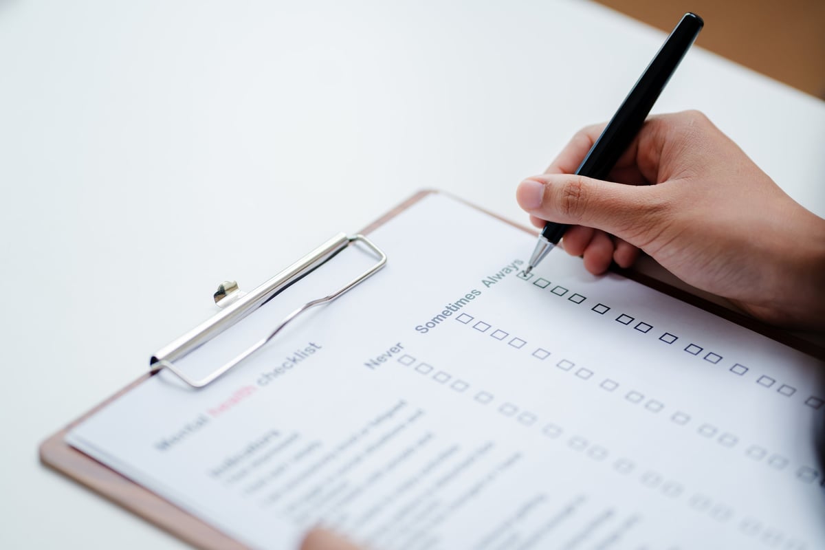 A person completing a structured self-assessment checklist on a clipboard